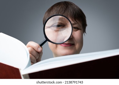 An Elderly Woman Reads With A Magnifying Glass In Her Hands.