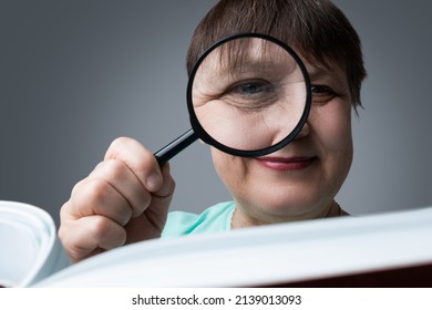 An Elderly Woman Reads With A Magnifying Glass In Her Hands.