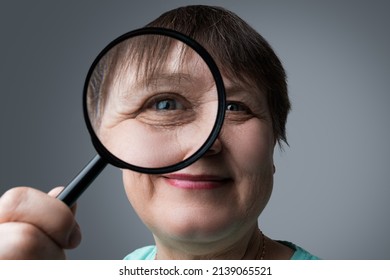 An Elderly Woman Reads With A Magnifying Glass In Her Hands.