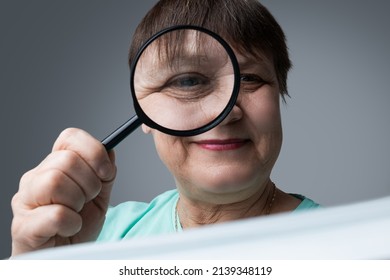 An Elderly Woman Reads With A Magnifying Glass In Her Hands.