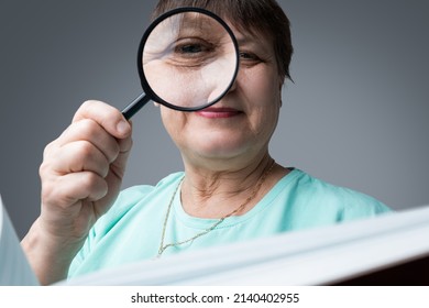 An Elderly Woman Reads With A Magnifying Glass In Her Hands.