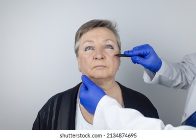 An Elderly Woman At The Reception Of A Facial Plastic Surgeon. Consultation On The Removal Of Age Wrinkles On The Face. The Doctor Shows What Procedures He Will Do. Mimic Wrinkles. Contour Plastic