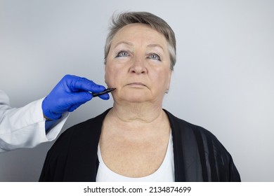 An Elderly Woman At The Reception Of A Facial Plastic Surgeon. Consultation On The Removal Of Age Wrinkles On The Face. The Doctor Shows What Procedures He Will Do. Mimic Wrinkles. Contour Plastic