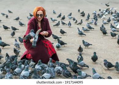 Elderly woman with red hair feeding pigeons in the park in Almaty - Shutterstock ID 1917144095
