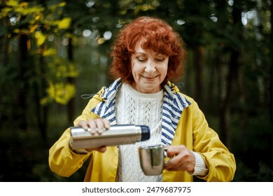 elderly woman with red hair pours coffee from a thermos in an autumn park. - Powered by Shutterstock