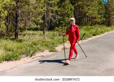 An Elderly Woman In A Red Tracksuit Walks With Nordic Walking Sticks In The Summer