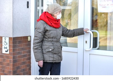 An Elderly Woman In A Respiratory Mask Reads An Ad On The Door Of A Closed Hospital.Seeking Medical Help From Older People. COVID-2019, Coronavirus Senior Health.