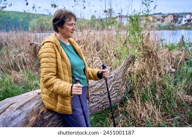 an elderly woman rests on the river bank after Nordic walking exercise - Powered by Shutterstock