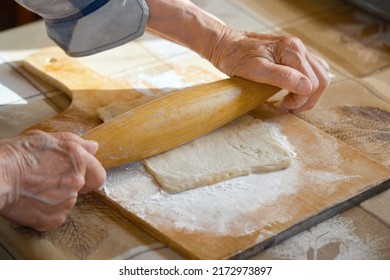 An Elderly Woman Rolls Out The Dough In Flour On A Cutting Board With A Rolling Pin. Woman's Hands With A Rolling Pin.