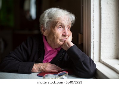 An elderly woman sadly looking out the window. Melancholy and depressed.