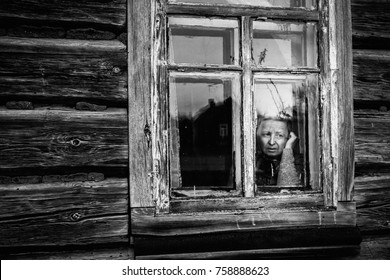 Elderly Woman Sadly Looking Out The Window. Black And White Photo. Old Granny. Wooden House