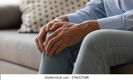 Elderly woman seated on couch touches knee suffers from repeated painful feelings on knee pain related to aging process close up image, tendonitis and arthritis diseases, joint degeneration concept