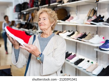 Elderly Woman Selecting New Sports Shoes In Shoe Shop.