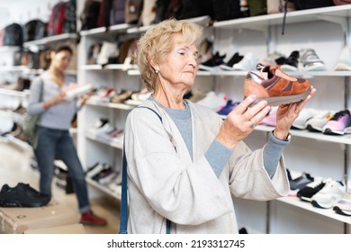 Elderly Woman Selecting New Sports Shoes In Shoe Shop.