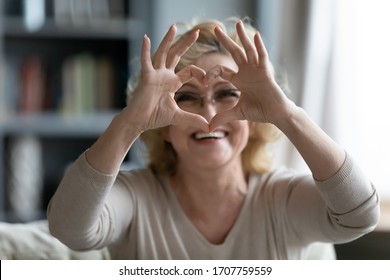 Elderly woman sit in living room connected fingers showing heart symbol close up, old people cardiovascular disease prevention treatment, health check-up, cardio vitamins, sign of kindness and charity