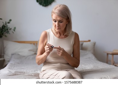 Elderly Woman Sit On Bed In Morning Holding Glucose Meter Lancets Needles Pricks Skin Obtain Blood Sample, Diabetic Patient Easily Do Check Up Control Of Blood Sugar Levels At Home, Diabetes Concept