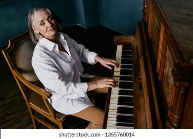An elderly woman sits at the piano in a white shirt