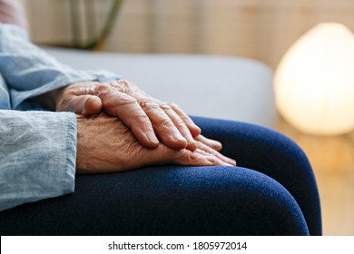 Elderly woman sitting alone at home, with hands folded on her laps. Senior old lady experiencing severe arthritis rheumatics pains, massaging, warming up arm. Close up, copy space, background