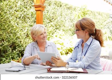 Elderly woman sitting in the garden with home health care nurse and consulting. Middle age caregiver holding in hand digital tablet and giving advice to her patient. 
