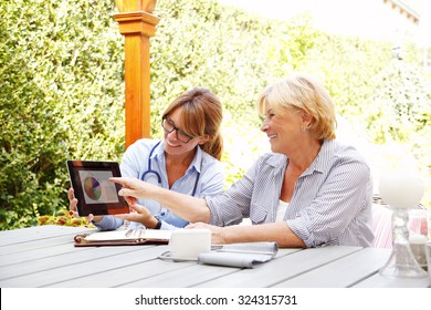 Elderly Woman Sitting In The Garden With Home Health Care Nurse An Using Blood Pressure. 