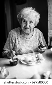 An elderly woman sitting at home eating at the table. Black-and-white photo.