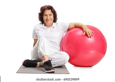 Elderly Woman Sitting On An Exercise Mat Next To A Pilates Ball Isolated On White Background