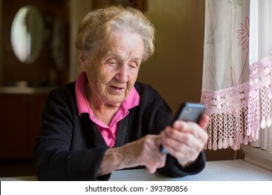 Elderly woman sitting at table typing on a smartphone. - Powered by Shutterstock