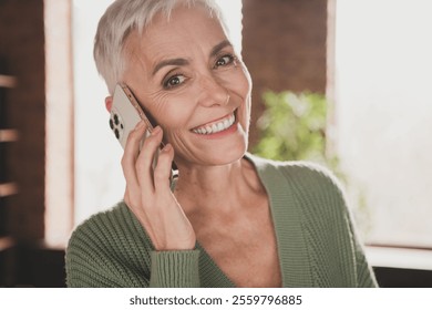 Elderly woman smiling warmly while talking on phone in a cozy living room ambiance - Powered by Shutterstock