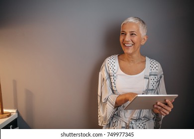 Elderly woman smiling while holding a tablet - Powered by Shutterstock