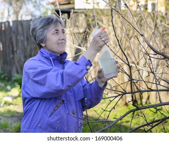 Elderly woman sprays trees in garden