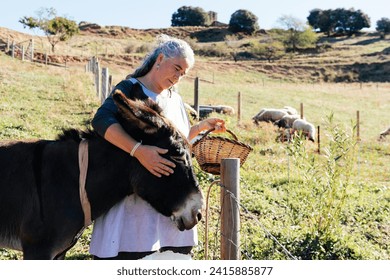 Elderly woman standing on grassy hilly valley in countryside and petting donkey in the head. - Powered by Shutterstock