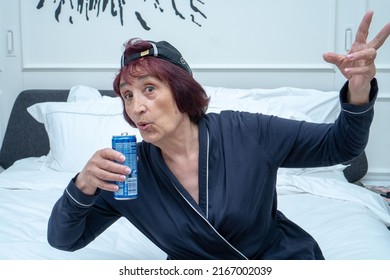 An elderly woman in a stylish Mercedes baseball cap drinks Pepsi and shows the symbol of victory with her fingers. Turkey, Istanbul, May 29, 2022.