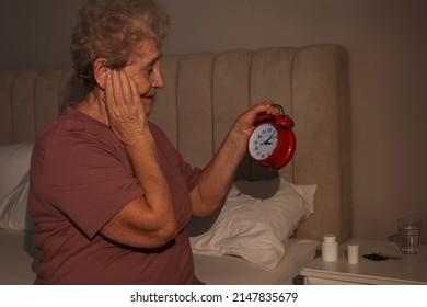 Elderly Woman Suffering From Insomnia Looking At Time On Alarm Clock In Bedroom