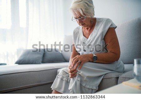 Elderly woman suffering from pain in knee at home. Senior woman holding the knee with pain. A mature woman massaging her painful knee.