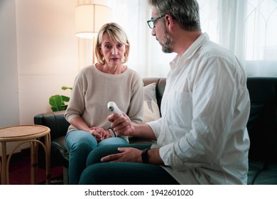 Elderly Woman Surprisingly Face While Looking Digital Thermometer In The Hand Of Her Husband After Found High Measurement Temperature. Health Care Self Check And Awareness At Home.