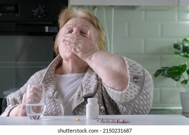 Elderly Woman Takes Pills In The Kitchen At Home. Single Retired Female Indoors. Old Age, Health Care, Retirement And People Concept