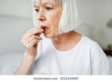 Elderly woman taking medication medicine pill. Senior woman with white hair taking a pill. Close-up of an elderly woman holding medication. Elderly woman in white shirt taking medicine pill. - Powered by Shutterstock