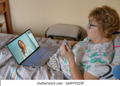 An Elderly Woman Is Talking With A Doctor On Skype. A Pensioner Suffers From A Respiratory Disease And Blows Her Nose. Online Consultation.