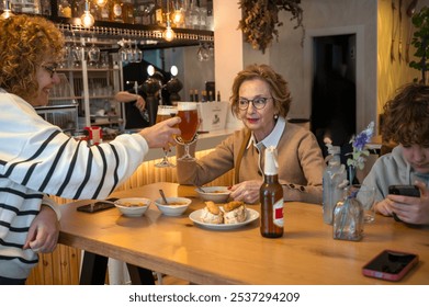 Elderly woman toasting with family at a cozy restaurant table - Powered by Shutterstock