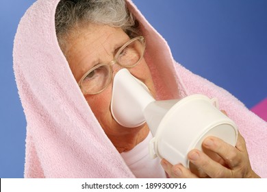 Une femme âgée avec une serviette au-dessus de la tête inhale la vapeur d'huile essentielle pour traiter les rhumes et le mal de gorge