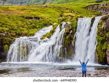 Elderly Woman -  Traveler Enthusiastically Raised Her Hands. Waterfall Kirkjoufellfoss. Summer In Iceland. Concept Of Exotic And Extreme Tourism 