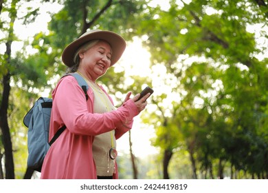 Elderly woman travels nature smiling happily Wear a hat and a backpack and carry a smartphone to check in at tourist attractions. Elderly tourists. Live a happy retirement life. - Powered by Shutterstock