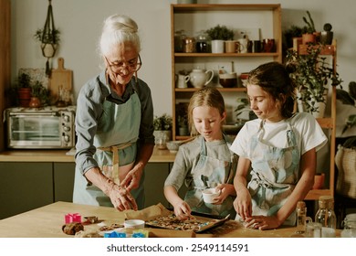 Elderly woman and two children decorating freshly baked cookies in cozy kitchen filled with plants and baking tools creating warm and joyful atmosphere - Powered by Shutterstock