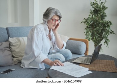 An Elderly Woman Uses A Laptop, Calculating Her Savings And Getting Frustrated With Debts And Huge Bills. Senior Female Looking For A Transcript Of Unpleasant Medical Tests And Expensive Treatment.