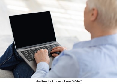 Elderly Woman Using Laptop With Blank Screen At Home, Making Video Call With Relatives Or Doctor, Mockup Image With Copy Space, Over Shoulder View