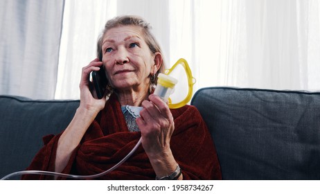 Elderly Woman Using Oxygen Inhaler While Having A Phone Call. Vulnerable Person During Covid Outbreak. High Quality Photo