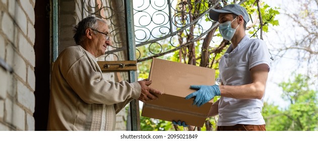 An elderly woman using a walker receives meals from a man working with a benevolent group delivering food to those who are at high risk because of the coronavirus COVID19. - Shutterstock ID 2095021849