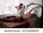 Elderly woman waking up in morning, sits on her bed and stretches after good night sleep, good mood, lady enjoying start of new day. Copy space