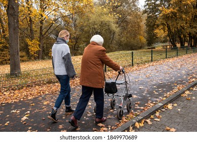 Elderly woman with walker taking a walk with caretaker wearing a mask to stay safe and prevent spreading of corona virus