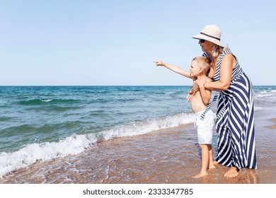 An elderly woman walks with a boy on the seashore. Grandmother and grandson stand on the sandy beach  and looks into the distance. Love and tenderness. Active lifestyle, health and relaxation. - Powered by Shutterstock